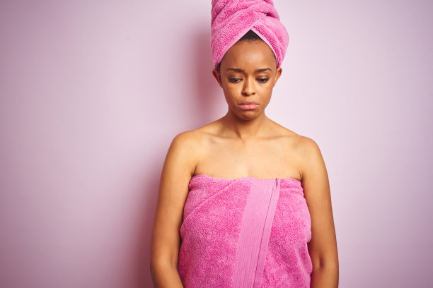 非裔美国女性浴后裹着浴巾，在粉色背景前沮丧哭泣，为痛苦而担忧图片下载