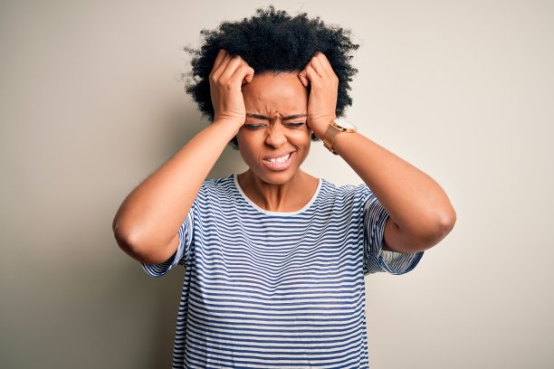 年轻漂亮的非裔卷发女子身穿条纹T恤，因头痛而痛苦、绝望和有压力，双手抱头。图片下载