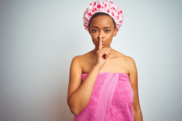 沐浴后身穿粉色浴巾的非裔美国妇女，要求安静，手指放在嘴唇上，保持沉默和秘密图片下载