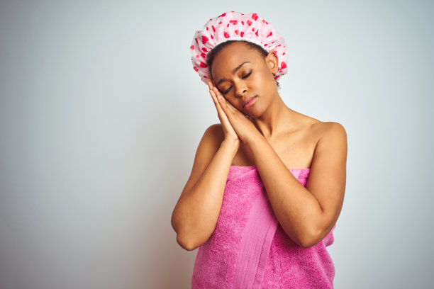 沐浴后身穿粉色浴巾的非洲裔美国妇女，在孤立的背景下疲惫地睡着，双手合十，闭着眼睛微笑图片下载