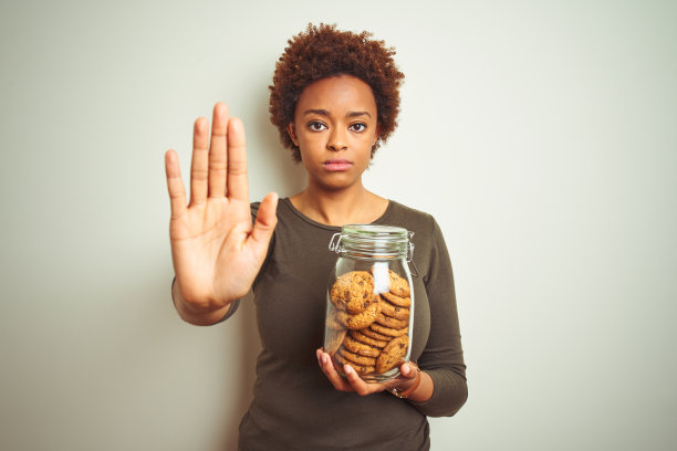 非裔美国妇女拿着一罐巧克力饼干，手掌打开做停止状，表情严肃自信图片下载