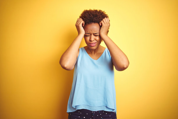 在黄色背景下，穿着优雅衬衫的非裔美国女性因头痛、绝望和压力而痛苦。双手抱头。图片下载