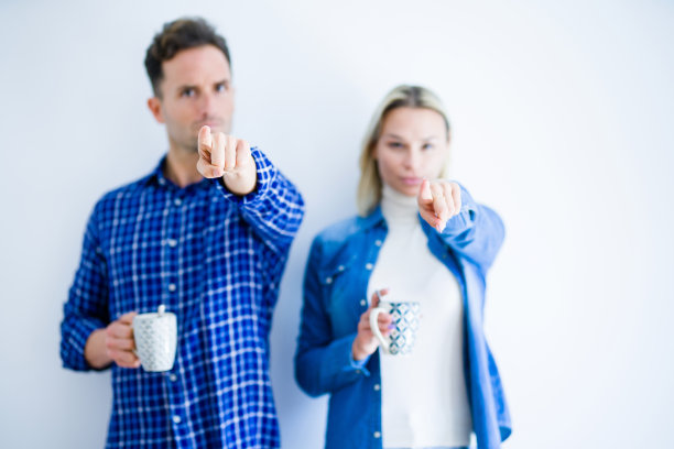 年轻漂亮的夫妇站在白色背景下喝咖啡，用手指指向镜头和观众，这是一个积极自信的手势。图片下载