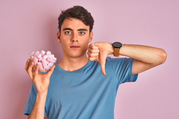 少年拿着棉花糖，粉色背景，面露不悦，表示拒绝图片下载