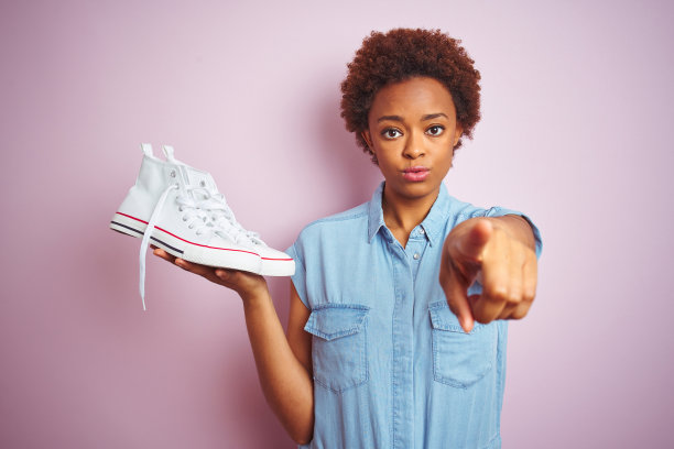 非裔美国女人拿着白色休闲运动鞋，指向镜头，手势积极自信图片下载