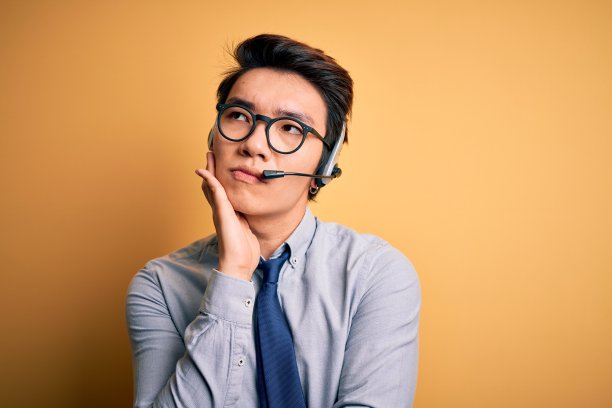 年轻英俊的中国呼叫中心话务员戴着眼镜，戴着耳机，双臂交叉，看起来疲倦和厌倦的抑郁问题。图片下载