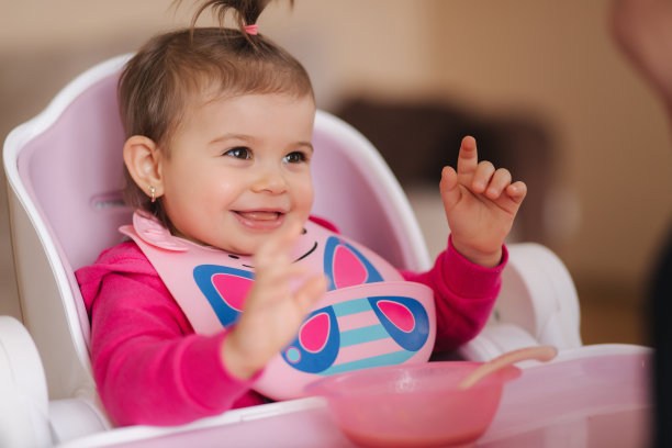 可爱的小女孩正在高椅上吃东西。家里微笑的小孩儿的肖像素材图片