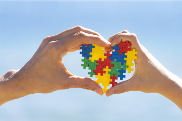 孩子和大人的手抱着彩色的心在蓝天的背景。世界自闭症宣传日的概念图片下载