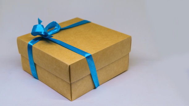 特写黄色礼盒与模糊的蓝色丝带在白色的背景。图片下载