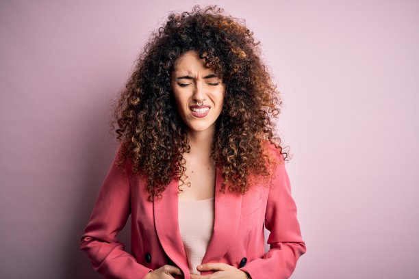 年轻美丽的女商人，卷着头发，穿着优雅的夹克服，手放在肚子上，因为消化不良，痛苦的疾病感觉不舒服。疼痛的概念。图片下载