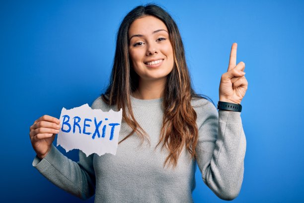 年轻漂亮的黑发女子拿着写有英国脱欧信息的纸，蓝色背景，惊讶地提出了一个想法或问题，快乐地指着手指，第一图片下载