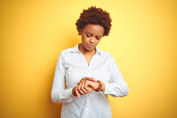 在黄色背景下查看手表的非裔美国女商人图片下载