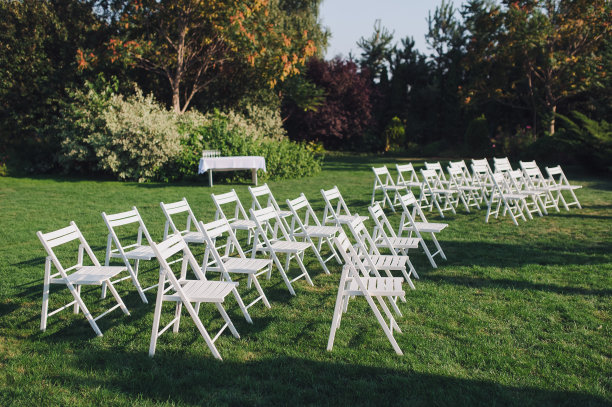 各种各样的白色木椅矗立在公园里，在绿色的草坪和草地上。婚礼装饰和细节。为婚礼做准备。举行婚礼，等候宾客。图片下载