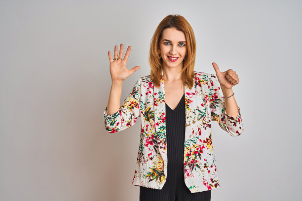 年轻的白人女商人身穿春季花卉夹克西装，在隔离背景前展示并用手指向上指着数字六，同时自信和快乐地微笑。图片下载