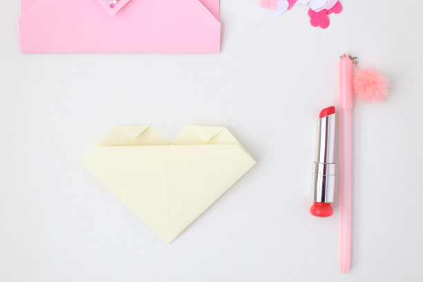 平铺:粉色信封，口红，钢笔，心形纸屑，用折纸技术折成心形的黄色纸。为情人节制作明信片。做你自己。系列图片图片下载
