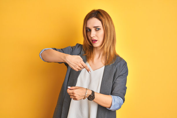 在黄色背景前查看手表的红发白人女商人，放松且自信图片下载