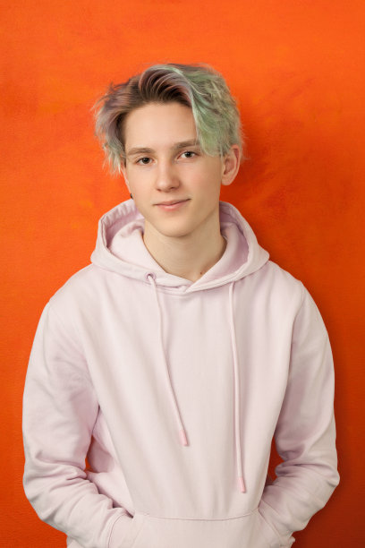 一个十几岁的男孩的工作室肖像与绿色的头发在一个橙色的背景图片下载