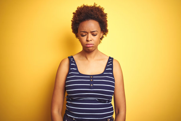 美丽的非洲裔美国妇女穿着夏季T恤，在黄色背景前感到沮丧和担忧，哭泣、愤怒和害怕，表情悲伤。图片下载
