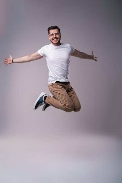 休闲装扮的英俊男人在灰色背景上庆祝跳跃图片下载
