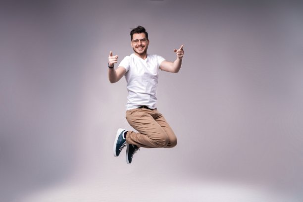 休闲装扮的英俊男人在灰色背景上庆祝跳跃图片下载