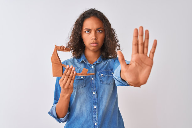 年轻的巴西女子拿着高跟鞋站在孤立的白色背景与开放的手做停止标志与严肃和自信的表情，防御手势图片下载