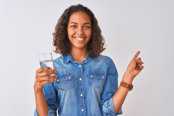 年轻的巴西女人拿着水站在孤立的白色背景非常幸福的指与手和手指的一边图片下载