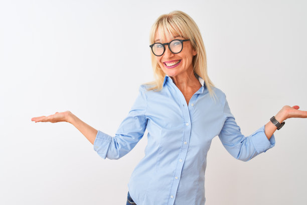中年女商人穿着优雅的衬衫和眼镜在白色背景前微笑，张开双手，展示和宣传比较与平衡图片下载