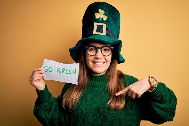 年轻美丽的女人戴着绿色的帽子和眼镜在圣帕特里克节庆祝与惊讶的脸指向自己的手指图片下载