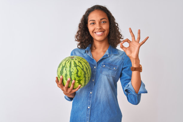 年轻的巴西女子拿着西瓜站在孤立的白色背景做ok手势用手指，优秀的象征图片下载