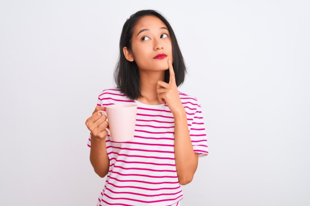 年轻美丽的中国女子喝着咖啡越过孤立的白色背景严肃地思考着问题，非常困惑的想法图片下载