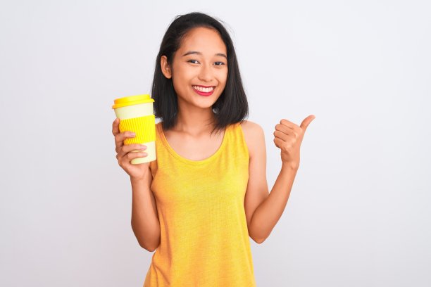 年轻的中国女人喝带走了一杯咖啡，在孤立的白色背景下，开心地笑着做ok的手势，用手指竖起大拇指，优秀的手势图片下载