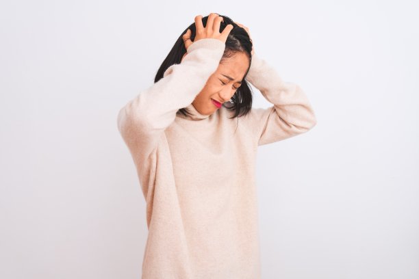 一名年轻的中国女子穿着高领毛衣，站在孤立的白色背景下，饱受头痛之苦，因为疼痛和偏头痛而绝望和压力。手放在头上。图片下载