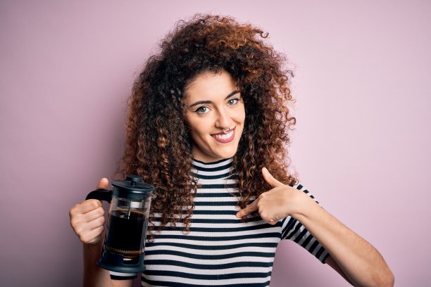 年轻漂亮的女人卷发和穿洞做咖啡拿着法国咖啡机惊讶的脸指向自己图片下载