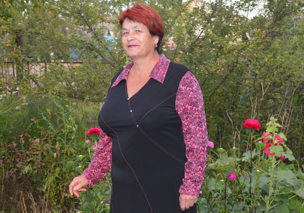 妇女穿着微笑，站在她的花坛附近与粉红色和红色紫苑。图片下载