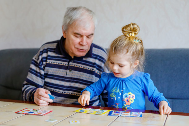美丽的蹒跚学步的小女孩和爷爷一起玩图画彩票桌上的纸牌游戏在家里。可爱的孩子和老人在一起玩。幸福的家庭在室内图片下载