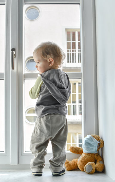 在冠状病毒和流感爆发期间，带着生病的泰迪熊的儿童站在窗口进行家庭隔离。2019冠状病毒病概念图片下载