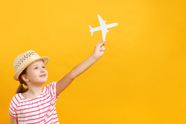 快乐积极美丽迷人的小女孩，戴着草帽，梦想着旅行，手里拿着纸飞机。黄色背景上的一个孩子的特写肖像。本空间图片下载