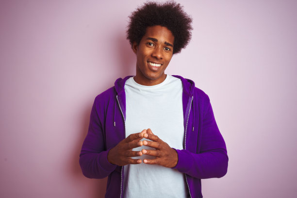穿着紫色运动衫的年轻非裔美国男子双手合十，面带微笑图片下载