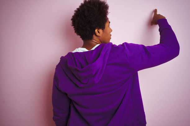 年轻的非洲裔美国人穿着紫色的运动衫站在孤立的粉红色背景摆出向后指向前面的手指手图片下载