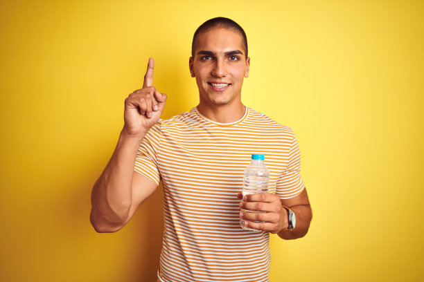 年轻英俊的男子拿着塑料水瓶在黄色孤立的背景惊讶与一个想法或问题指向手指与快乐的脸，一号图片下载