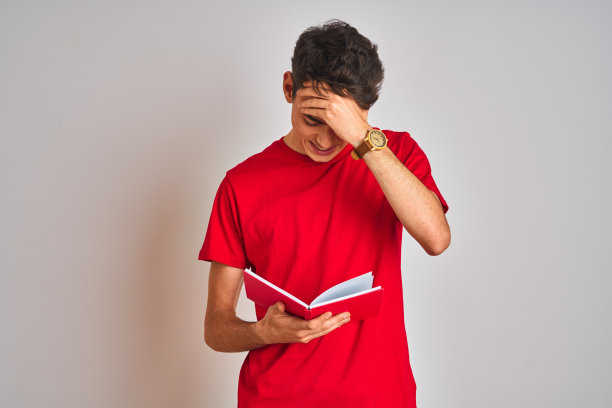 十几岁的学生男孩读一本书在孤立的背景强调与手头上，震惊与羞愧和惊讶的脸，愤怒和沮丧。为错误而恐惧和不安。图片下载