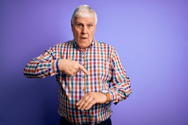 资深英俊的白发男子穿着休闲彩色衬衫越过孤立的紫色背景匆忙指向手表时间，不耐烦，心烦和愤怒的期限延误图片下载