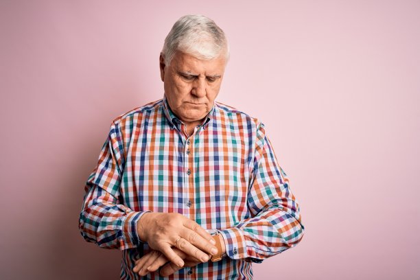 老帅白皙男子穿着休闲彩色衬衫，越过孤立的粉红色背景查看手表上的时间，轻松和自信图片下载