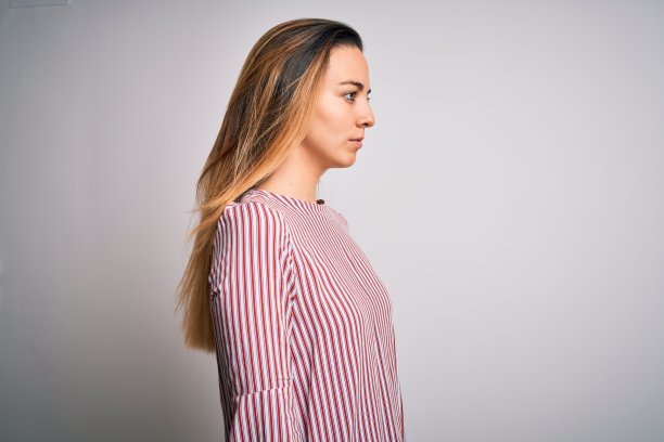 年轻美丽的金发女子与蓝色眼睛穿针t恤在白色的背景看向一边，放松的侧面姿势与自然的脸自信的微笑。图片下载