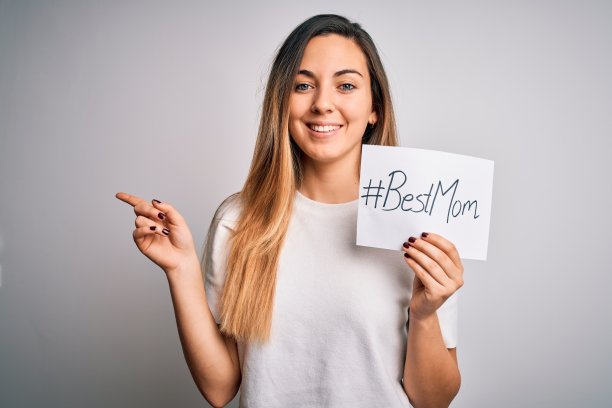 年轻漂亮的女人拿着纸和最好的妈妈短信庆祝母亲节非常快乐，用手和手指指着一边图片下载