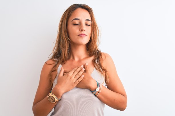 年轻的红发女子穿着休闲t恤站在白色孤立的背景微笑，双手放在胸前，闭上眼睛和感激的手势在脸上。健康的概念。图片下载