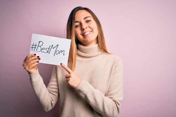 年轻漂亮的女人拿着纸和最好的妈妈短信，用手和手指指着庆祝母亲节非常快乐图片下载