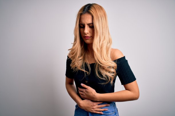 年轻美丽的金发女子穿着休闲t恤站在孤立的白色背景与手胃，因为消化不良，痛苦的疾病感觉不舒服。疼痛的概念。图片下载