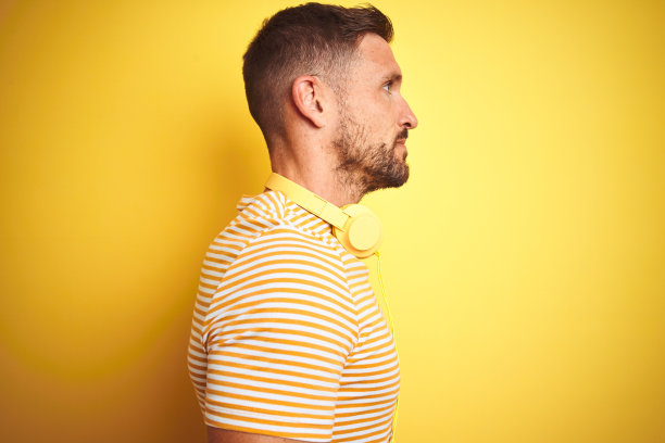 年轻英俊的男子戴着耳机听音乐，黄色孤立的背景看向一边，放松的侧面姿势与自然的脸与自信的微笑。图片下载