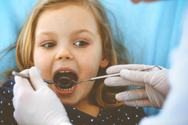 小女孩张大嘴巴坐在牙科椅上接受医生的口腔检查。拜访牙医的办公室。医学概念。健美的照片图片下载